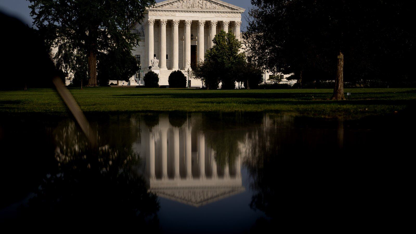 The United States Supreme Court building is reflected in a pool of water as it stands in the background of the image.