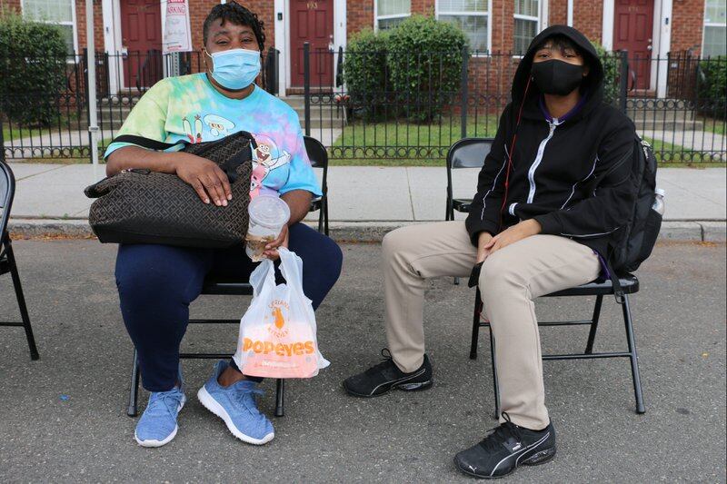 A mother and daughter, wearing masks, sit on folding chairs outside a pop-up COVID vaccination clinic in Newark.