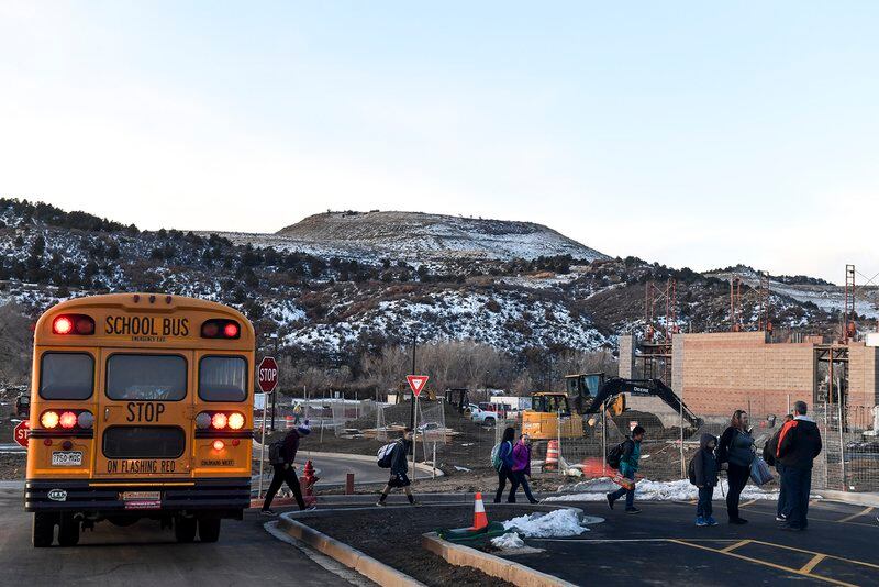 A yellow school bus drops off students with a mountain in the background.