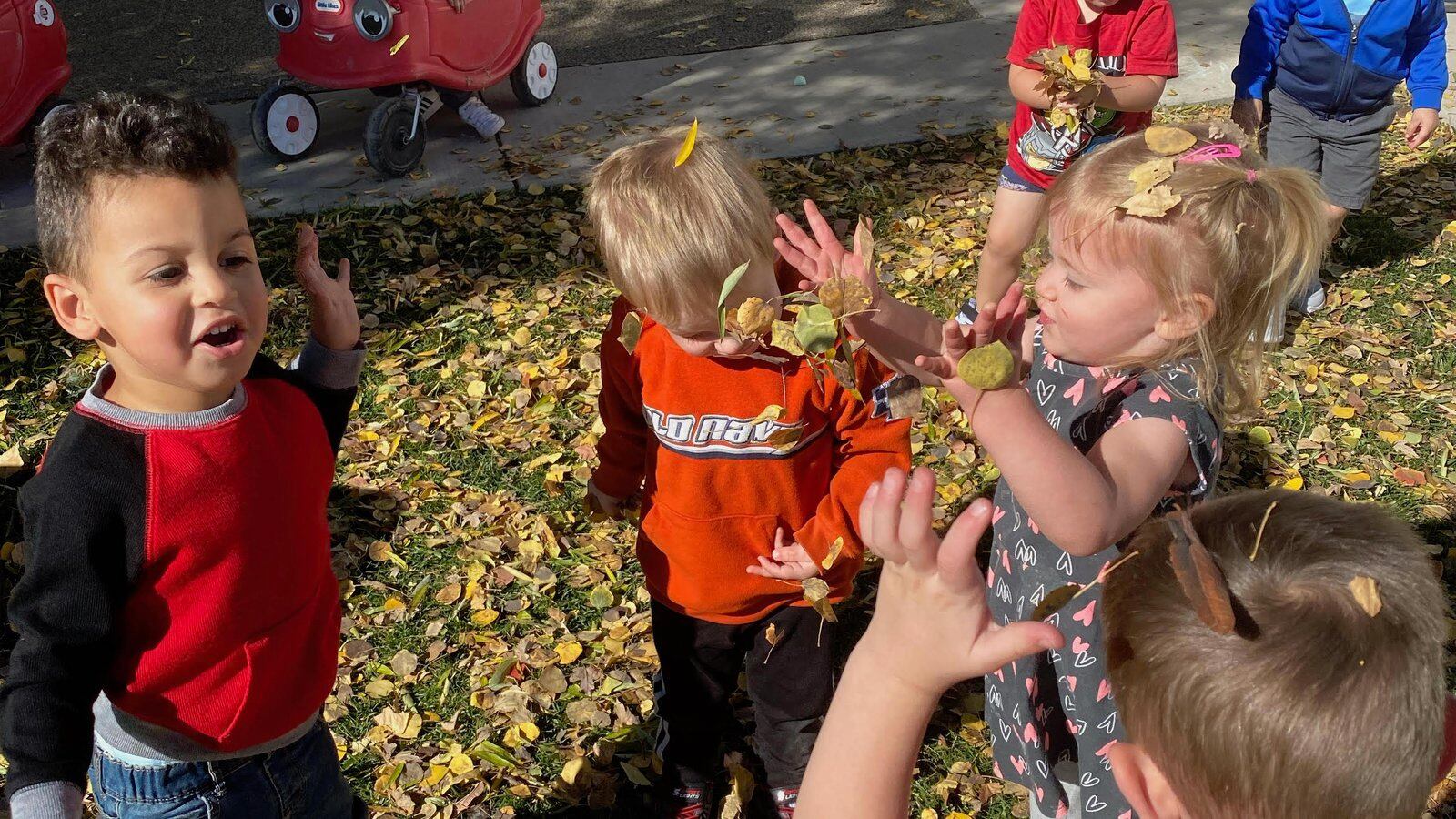 Six preschool children play in fall leaves