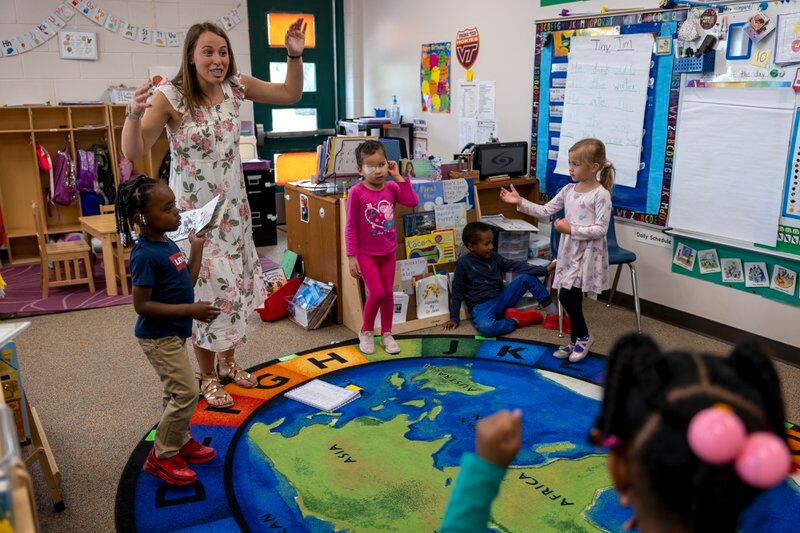 A preschool teacher in a floral dress makes a funny face during a a circle activity with several students.