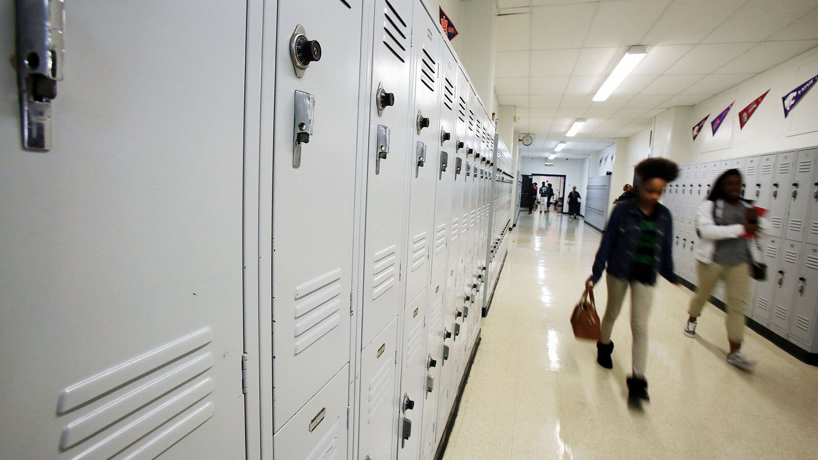 Students walk past white lockers in a school hallway