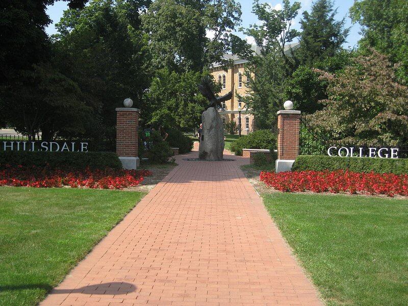 Open entrance gate to a college campus with bricked walkway that leads to a courtyard with a bronze statue of an eagle
