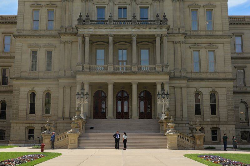 A man and a woman stand in front of the steps of the Michigan Capitol in Lansing.