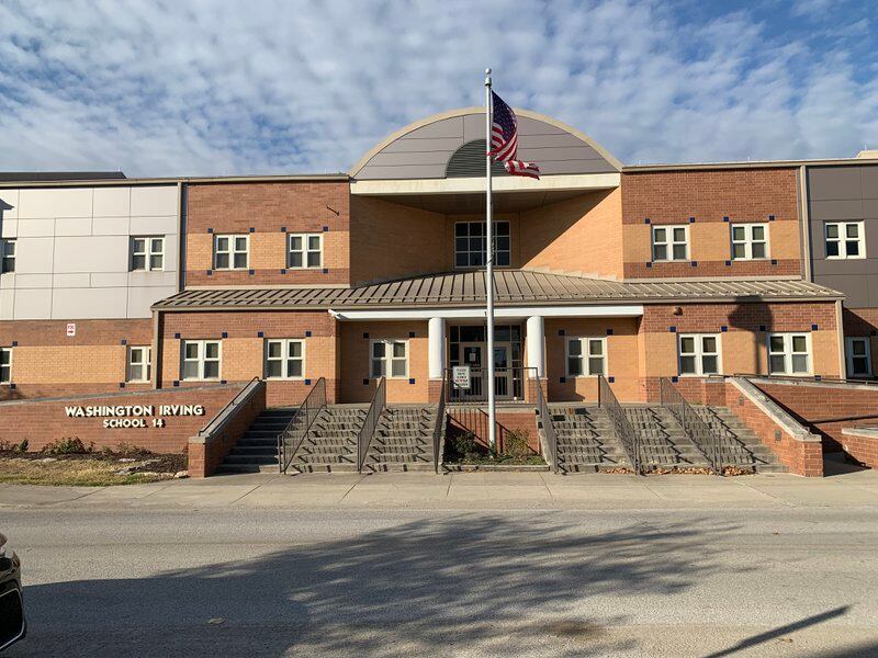 A brick building with an American flag sits behind a set of stairs. On the left of the stairs are white letters that read “Washington Irving School 14.”