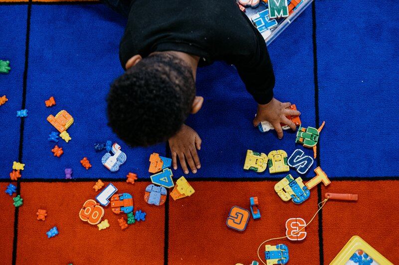 A young student kneels on a mat playing with multicolored toys