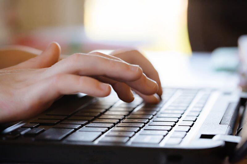 A child’s hands typing on a black laptop keyboard.
