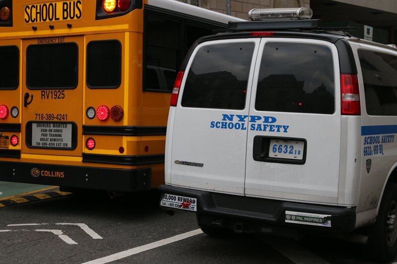 The back of a yellow school bus sits next to the back of a white police van.