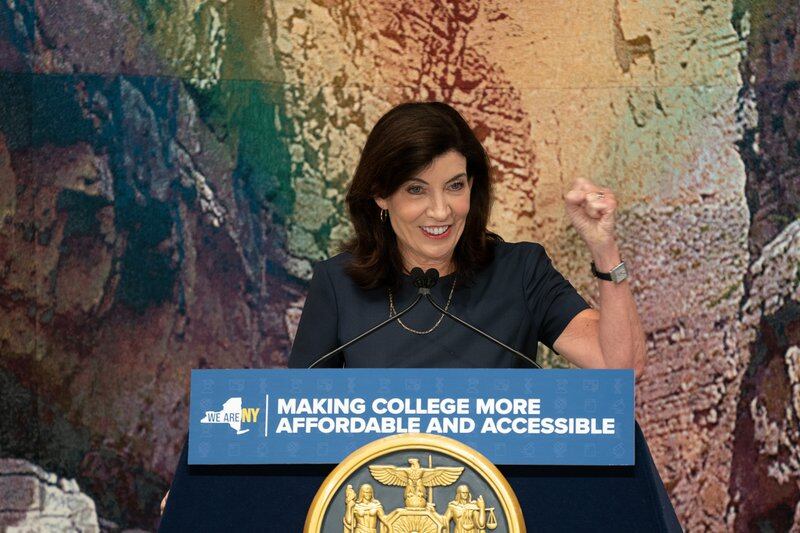 A smiling woman stands at a lectern with her fist held up.