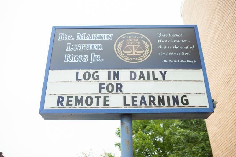 A sign outside Dr. Martin Luther King, Jr. Academy of Social Justice that reads: log in daily for remote learning.