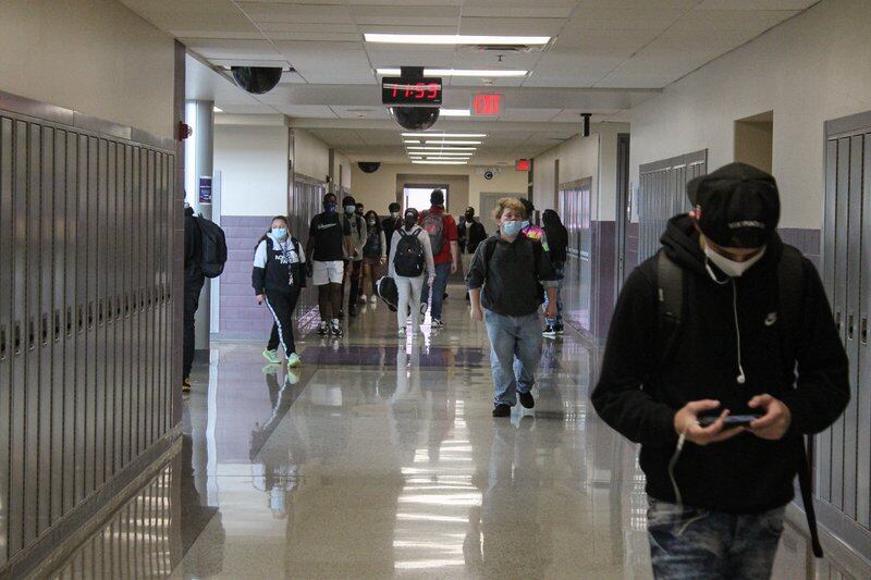 Students walk through the hallway in a high school, all wearing masks due to COVID protocols.