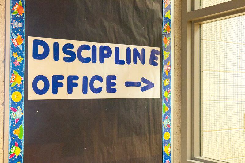 A sign reads “DISCIPLINE OFFICE” on a board with black paper next to a school office’s windows.