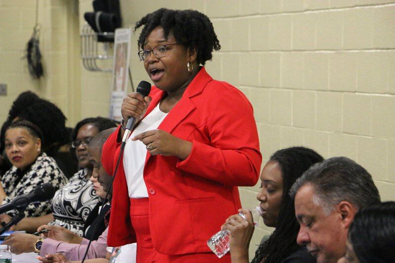 Newark Board of Education member A’Dorian Murray-Thomas. wearing a red suit, speaks while holding a microphone.