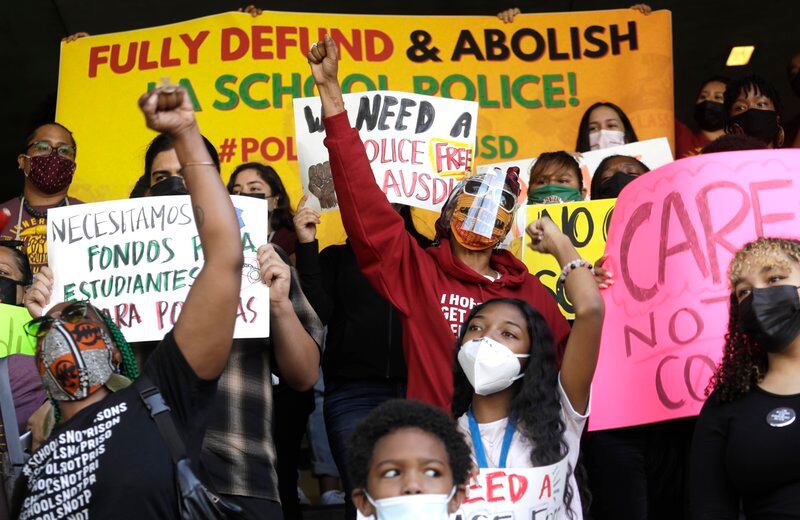 Several protestors wearing protective masks protest the presence of police in schools. A large yellow sign behind them reads “FULLY DEFUND &amp; ABOLISH LA SCHOOL POLICE!”