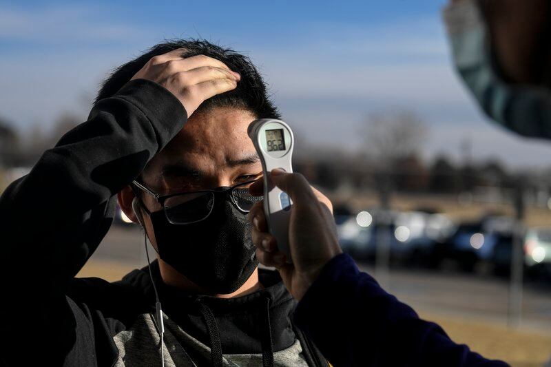 A teenage boy gets his temperature checked with a forehead thermometer outside a school.
