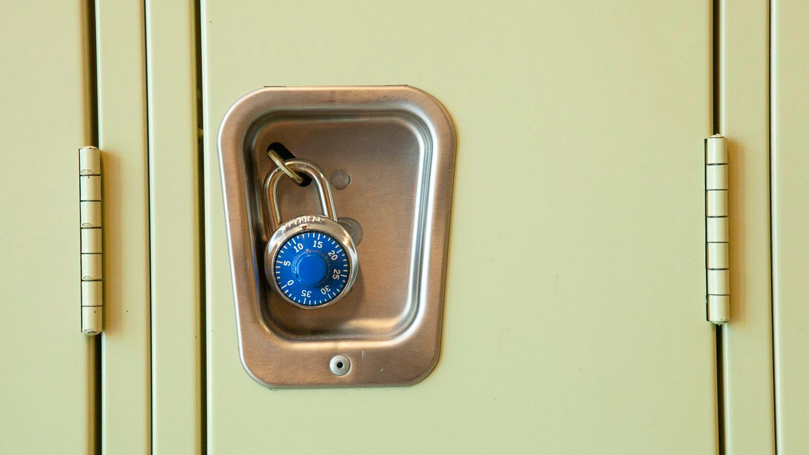 A close of image of a yellow high school locker with a blue pad lock. 