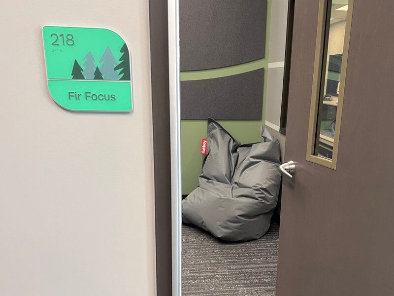 A grey wall and brown door open up to a bean bag that sits on the floor in the corner of the room.  