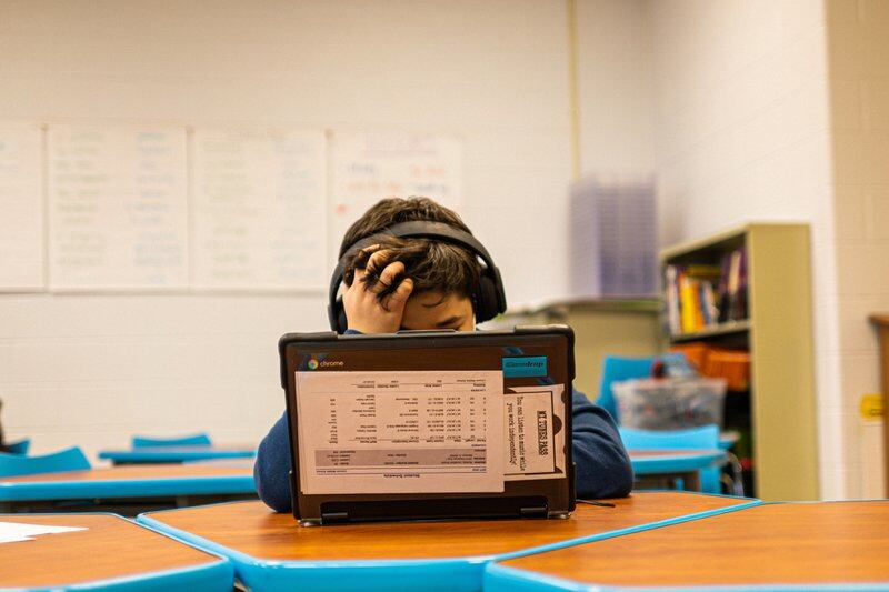 A student, wearing headphones, works at his laptop while running his fingers through his hair.