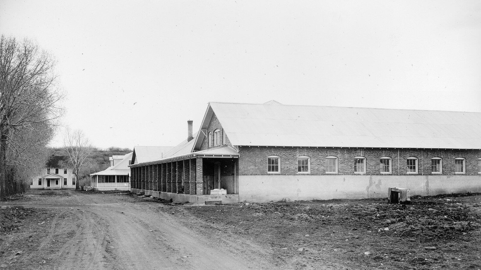 A black and white photograph of a building next to a dirt road. 
