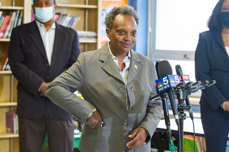 Mayor Lori Lightfoot stands by microphones while placing a face mask into her jacket pocket.