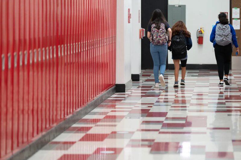 Three students walk next to red lockers in the hallway at Lake View High School in Chicago.