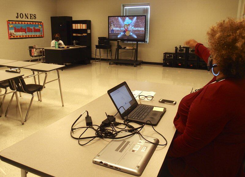 Teachers talk about an online class from across the room to social distance