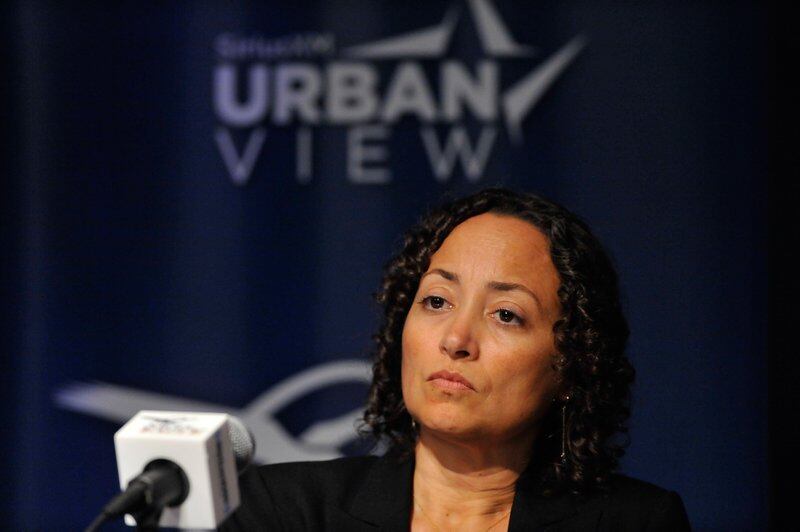 Catherine Lhamon sits at a podium, with a white microphone in front of her as a banner reading “Urban View” hangs behind her.