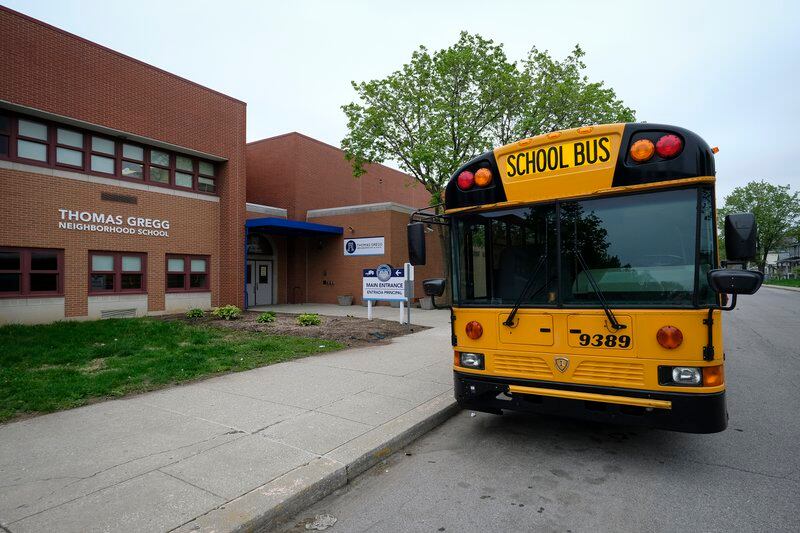 A yellow school bus is parked in front of the brick building of Thomas Gregg Neighborhood School in Indianapolis, Ind.