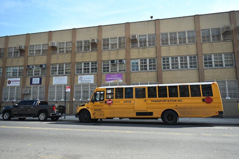 A yellow school bus and truck are parked on the street in front of the Brooklyn Democracy Academy in New York City.