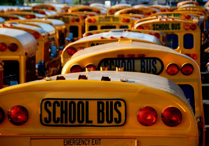 More than a dozen school buses are parked by each other.