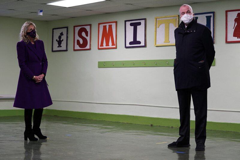 (Left to right) Dr. Jill Biden, wearing a mask and dark purple coat, stands next to New Jersey Governor Phil Murphy, who is wearing a mask and black coat. The wall behind reads “SMITH” in large multi-colored block letters.