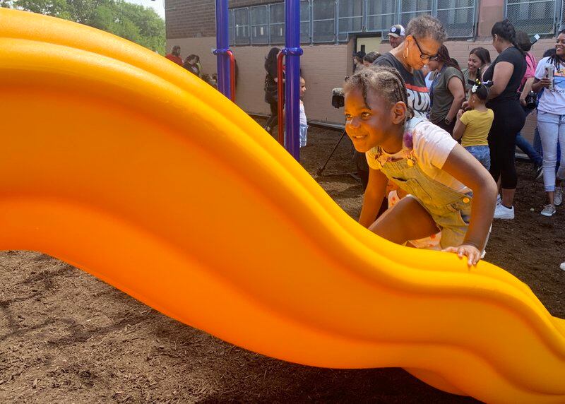 a girl in shorts overalls and a white t-shirt climbs up a bright yellow slide