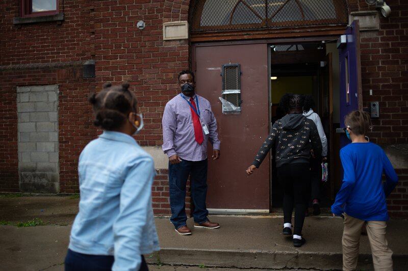 A teacher watches as students make their way into the brick facade of their school.