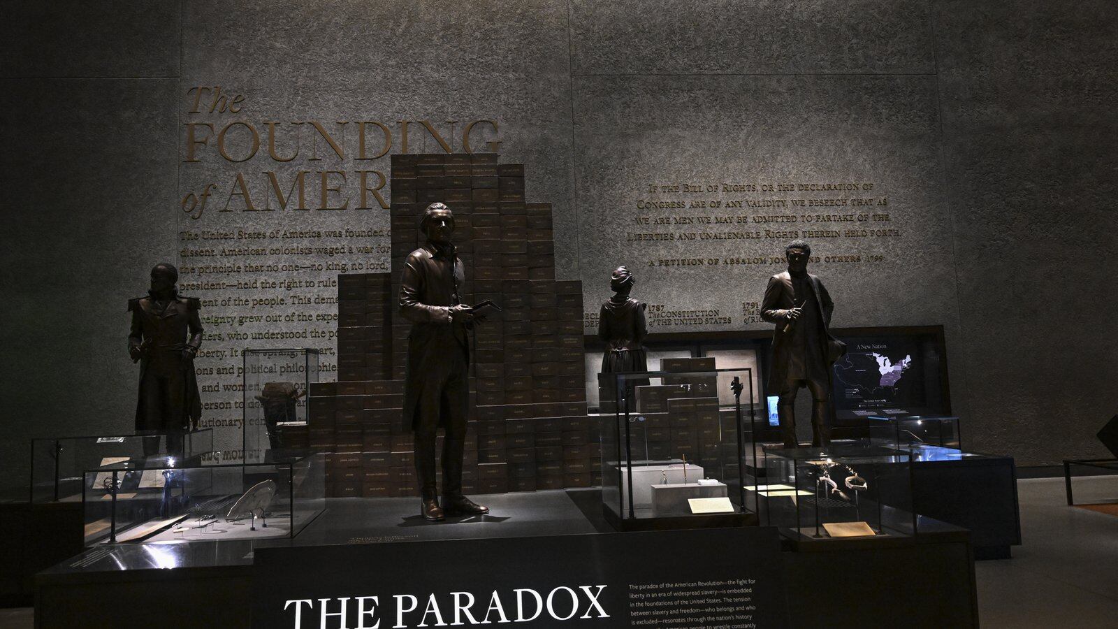 A hunk of wood and metal bar sit in the center of a near pitch dark room in the basement of the National Museum of African American History and Culture. A sign reads, “The Paradox of Liberty.”