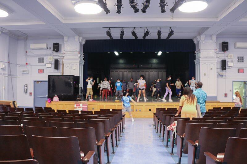 Students stand on a stage in an auditorium.