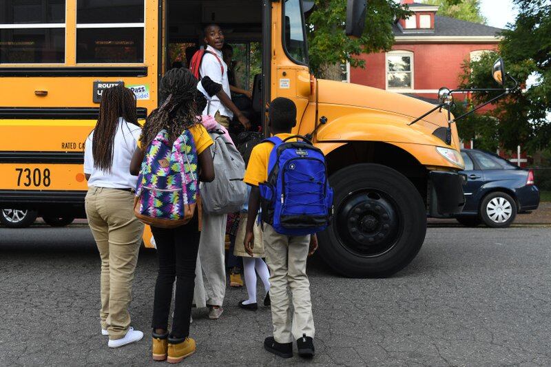 A group of students with their backs to the camera board a yellow school bus.