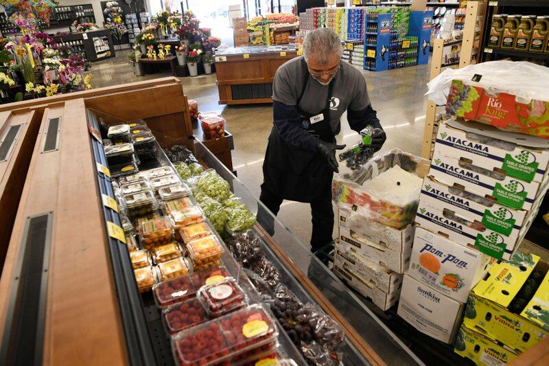 A man stocks grapes and strawberries in a grocery store.