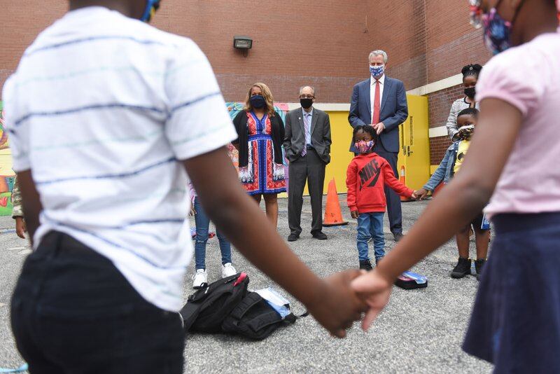 Two students holding hands in the foreground, while in the back stand Mayor Bill de Blasio and Schools Chancellor Meisha Porter.