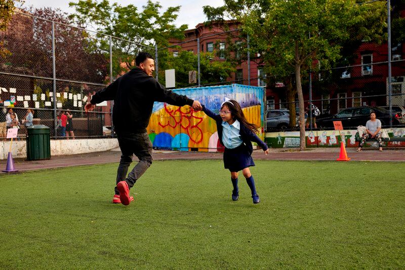 A father and daughter play on a small turf field together.