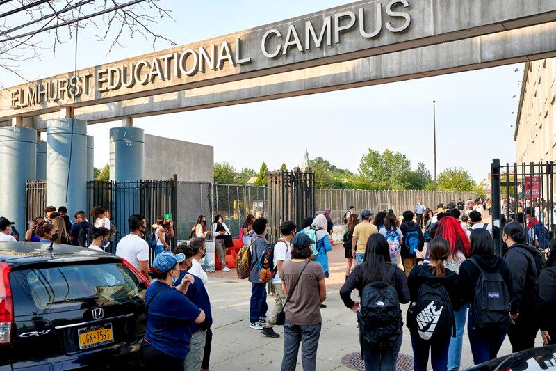 A crowd of students gathers outside a gray concrete high school building. 