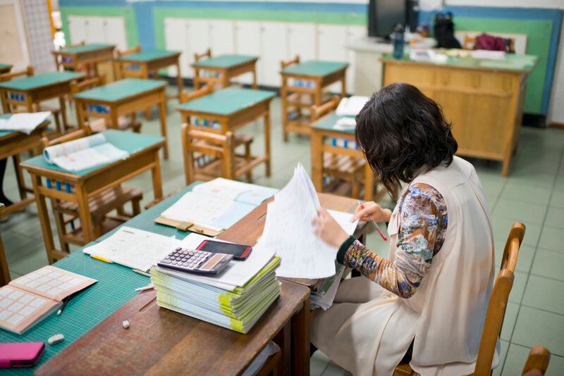 A teacher grades papers in an empty classroom.