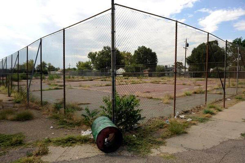 The corner of a chain link fence enclosing pavement and weeds at the former Adams City High School in Adams County, Colo.