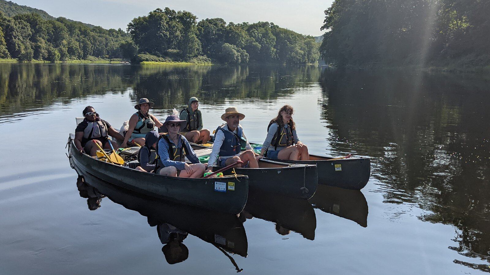 A group of teachers wearing lifejackets sit in three canoes