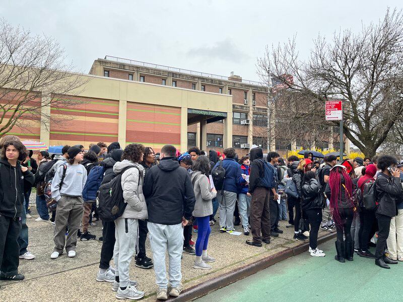 Hundreds of high school students stand outside of a school building.