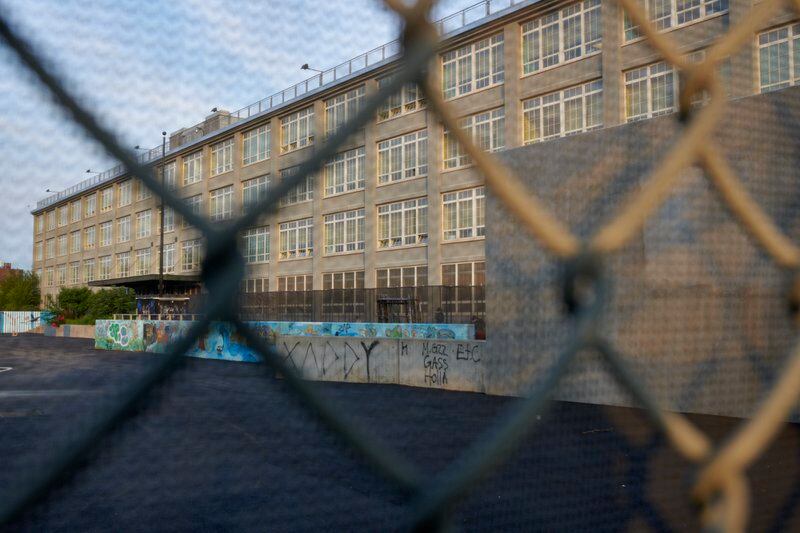 The facade of Pan American High School in Elmhurst is seen behind a chainlink fence as the sun shines on the building.
