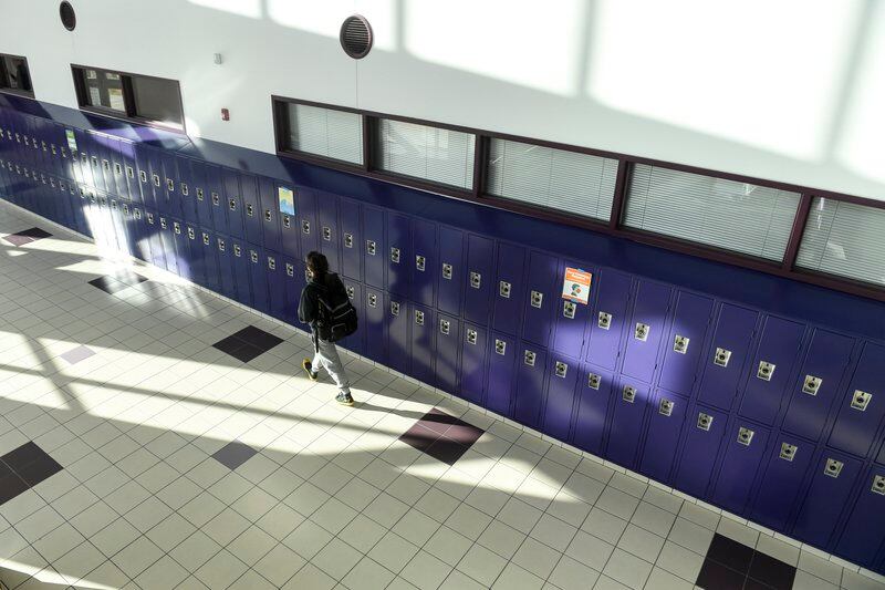 A high school student walks in an empty hallway past a row of purple lockers.