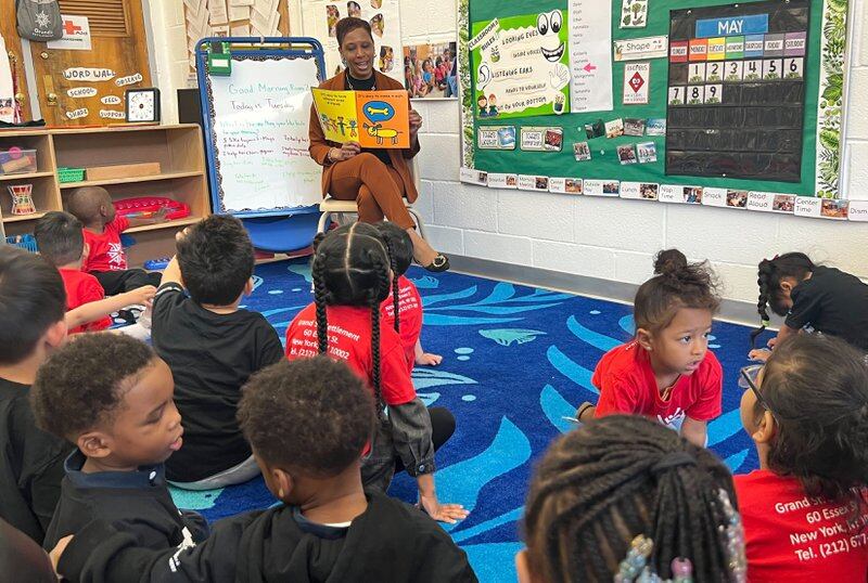 woman in orange pantsuit reads to students