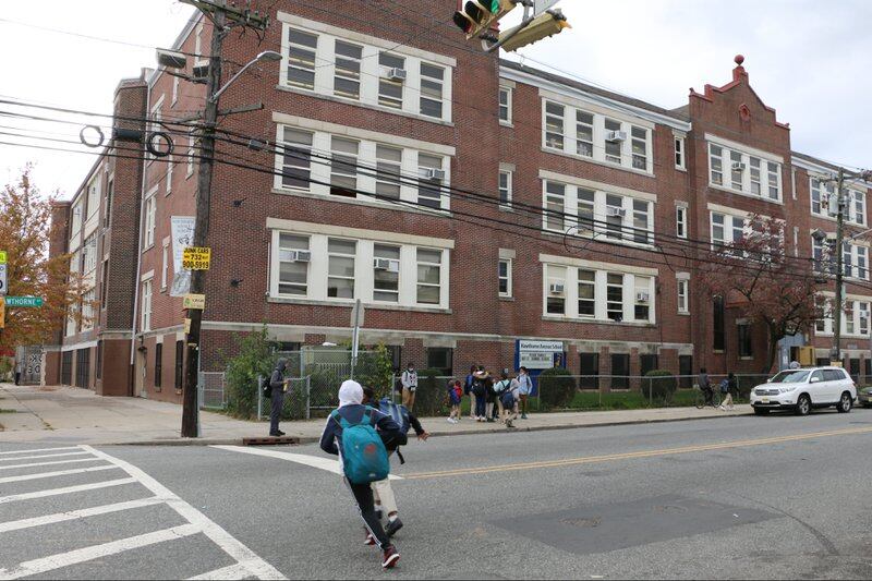 A boy with a blue backpack runs across the street in front of a school building in Newark.