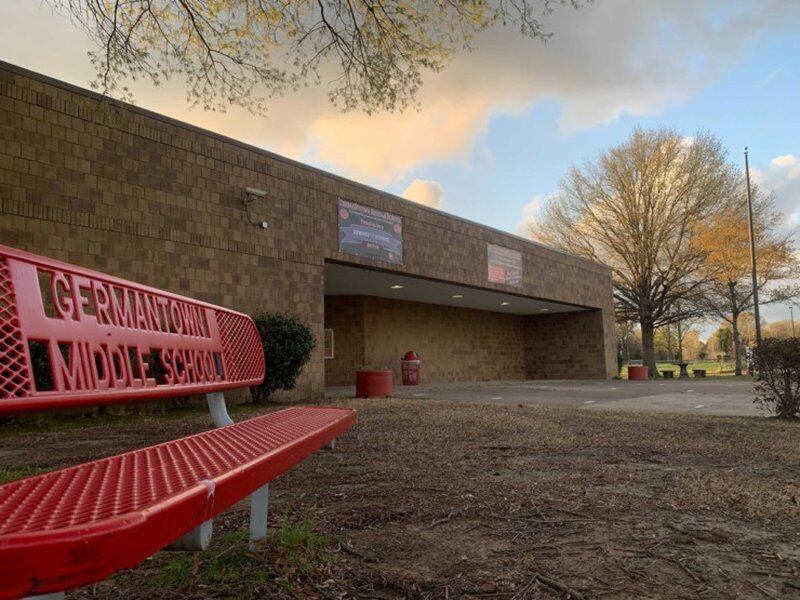An empty bench, bearing the Germantown Middle School name, sits outside of a school building.