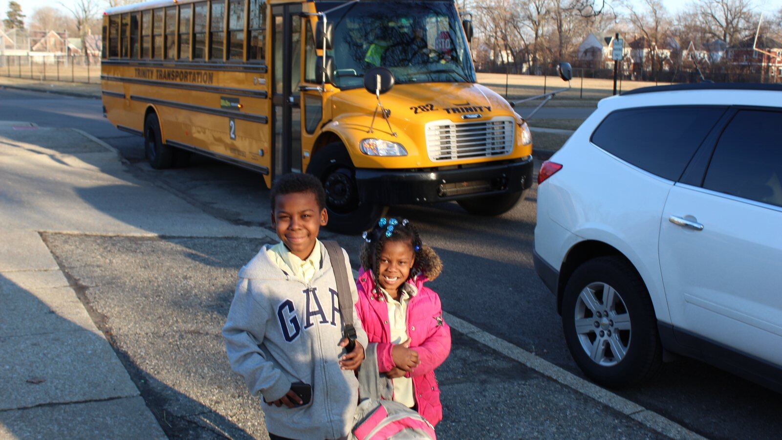 Two young children stand in front of a yellow school bus.